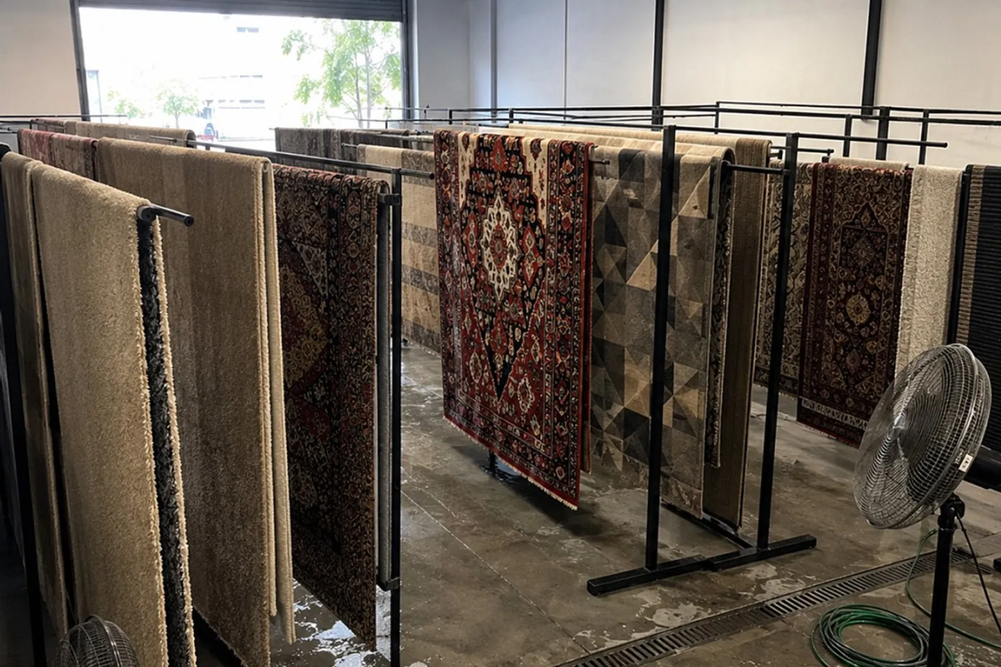 Fileiras de tapetes pendurados nos varais da oficina da Flex Clean